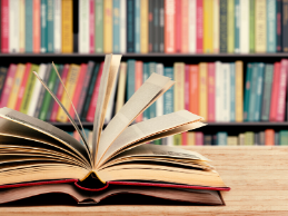 photo of open book on a table in front of a full bookcase