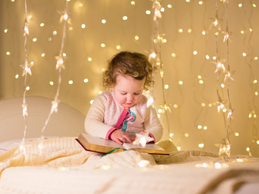 photo of child reading a book with holiday lights in the background